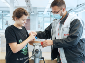 An der Werkbank entgraten Johanna (13) und Brose Auszubildender Blerton ein Kunststoff-Herz aus dem 3D-Drucker für einen Schlüsselanhänger (©Brose)
