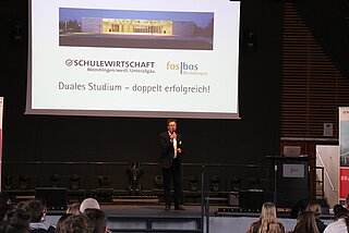 Mann auf der Bühne mit Präsentation im Hintergrund