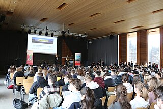 Überblick von hinten in einen voll besetzten Saal mit Bühne