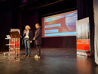 Bühne mit zwei Frauen die am Podium sprechen